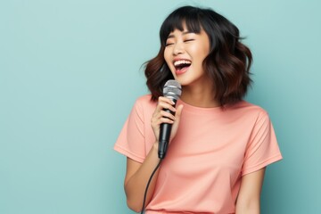 Portrait of a satisfied asian woman in her 20s dancing and singing song in microphone over solid color backdrop