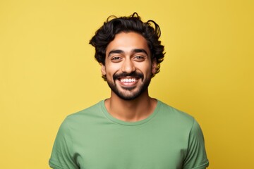 Obraz premium Portrait of a cheerful indian man in his 20s smiling at the camera while standing against solid color backdrop