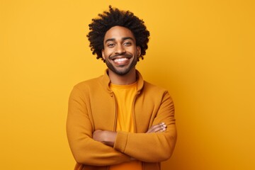 Obraz premium Portrait of a grinning afro-american man in his 20s with arms crossed while standing against solid color backdrop