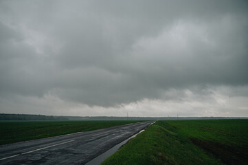 road in a field against the backdrop of a large dark cloud with rain