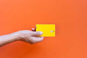Hand holding yellow credit card on orange background top view contact less payment concept