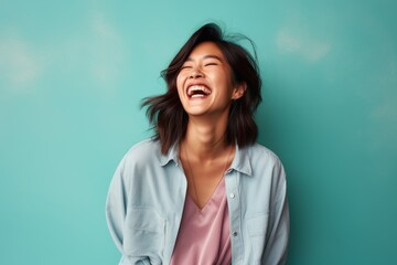 Portrait of a satisfied asian woman in her 30s laughing in solid pastel color wall