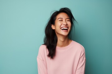 Portrait of a satisfied asian woman in her 30s laughing isolated on solid pastel color wall
