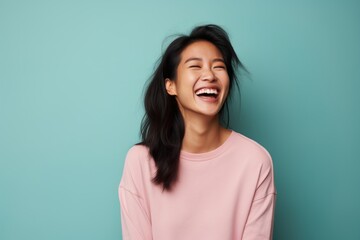 Fototapeta premium Portrait of a satisfied asian woman in her 30s laughing isolated on solid pastel color wall