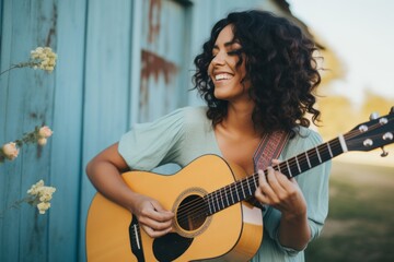 Portrait of a smiling woman in her 30s playing the guitar isolated on solid pastel color wall