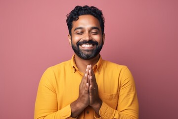 Portrait of a happy indian man in his 30s joining palms in a gesture of gratitude isolated on solid...