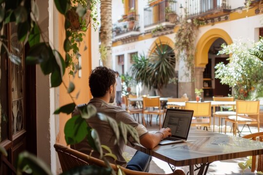 digital nomad expat working on laptop at cafe terrace or coworking in a narrow street of a town in Spain in summer - Powered by Adobe