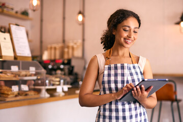 Young Woman Using Digital Tablet Wearing Apron Working In Coffee Shop Or Cafe