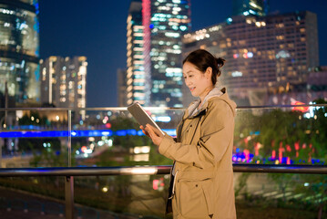 Professional Woman Engaged with Tablet in Urban Night Setting