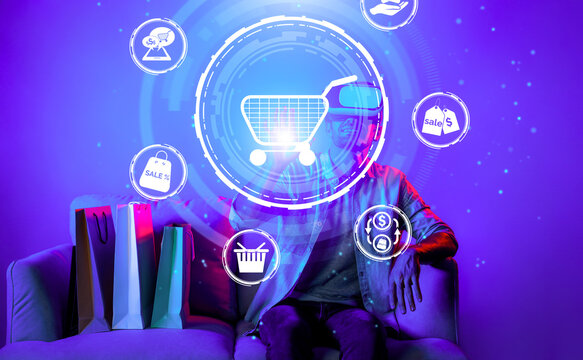 Happy man using VR headset and shopping online while sitting at sofa with shopping bags. Smart person looking at online market hologram and icon with neon background. Innovation technology. Deviation.