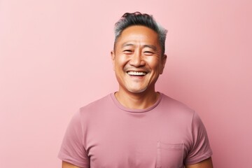 Portrait of a happy asian man in his 40s smiling at the camera in solid pastel color wall