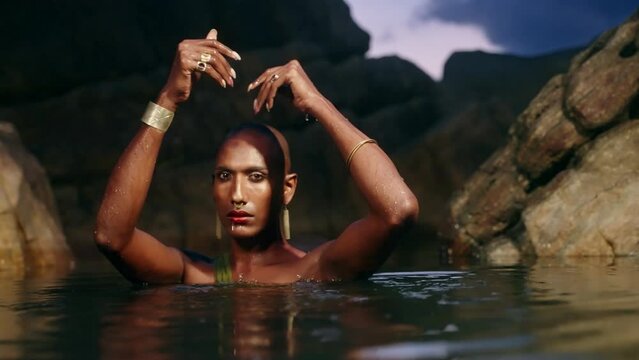 Non-binary black person stands chest deep in the middle of still water inside scenic creek at night. Lgbtq ethnic graceful fashion model poses immersed in crystal clear pond at exotic location