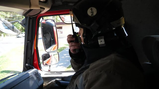 Male firefighter talks on walkie-talkie while driving on fire engine to an emergency. Professional fireman in full equipment speaks on radio communication during riding on big truck to place of a fire