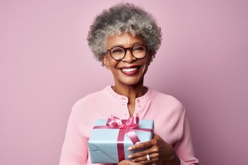 Portrait of a glad afro-american woman in her 50s holding a gift in front of solid pastel color wall