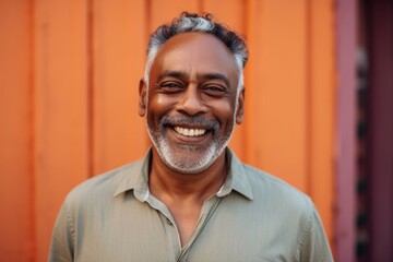 Obraz premium Portrait of a happy indian man in his 50s smiling at the camera while standing against solid pastel color wall