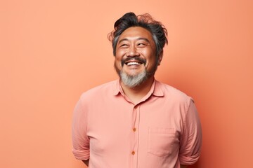 Obraz premium Portrait of a jovial asian man in his 50s smiling at the camera in solid pastel color wall