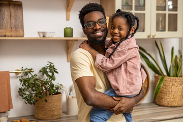 Smiling black man holding his little daughter in kitchen interior