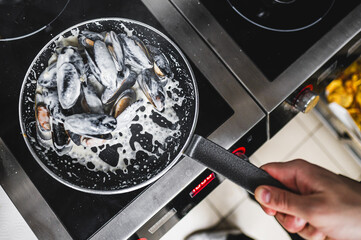 Fresh mussels cooking in a pan with creamy sauce on an induction stove, kitchen background