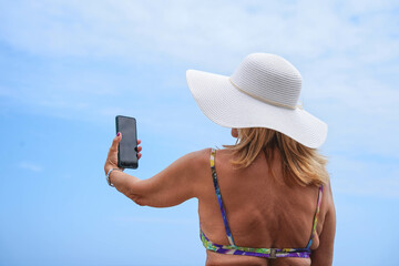 Rear view of caucasian tourist wearing a hat taking a photo with her mobile. Summer vacations