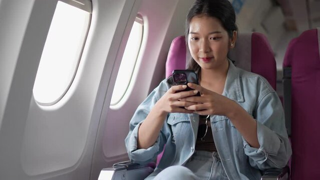 An Asian female tourist is using a smartphone to play games to pass the time while traveling abroad by plane
