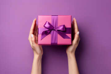 romantic purple or magenta background with woman hands holding a wrapped gift box seen from above for a birthday
