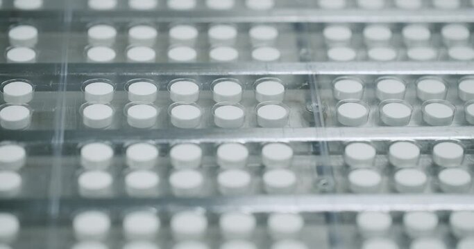 White pills moving on metal automatic line in workshop of pharmaceutical factory. Process of production of pills, drugs.Industrial pharmaceutical concept.Closeup view of drugs move along conveyor belt