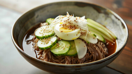 Tasty korean cold noodles with cucumber, boiled egg, and sesame seeds served in a wooden bowl