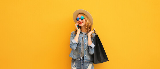 Beautiful young woman calling on smartphone with black shopping bag, summer hat on yellow background