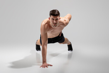 A fit young man is captured performing a plank exercise in a minimalist studio bathed in sunlight....