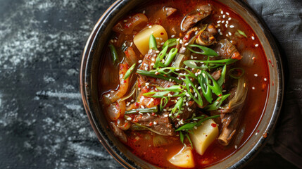 Spicy korean beef soup with spring onions in a rustic bowl on a dark background, full of authentic flavors