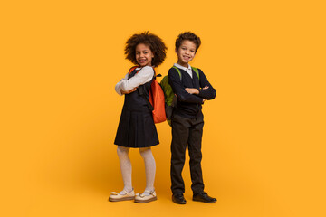 Two African American children dressed in school uniforms are standing on a bright yellow...
