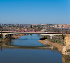 Obraz premium A person slides down a tourist zip line over the great Tagus River in the city of Toledo, Spain. Next to the Alcantara bridge.