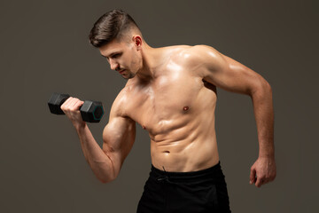 A man is lifting a dumbbell in front of a plain gray background. He is focused and determined,...