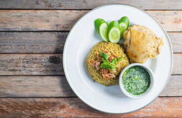 Delicious chicken biryani served with fresh cucumber slices and a side of green sauce on a rustic wooden table.