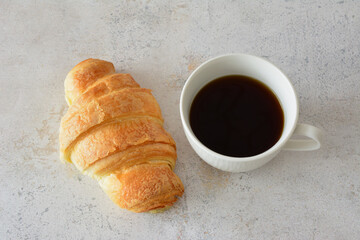 a cup of coffee next to a croissant top view