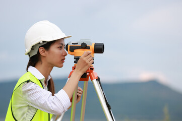 Portrait beautiful Asian construction engineer with a green safety vest hard hat and level survey...