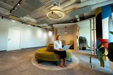 Modern office lounge with green circular seating and woman working on laptop during daytime