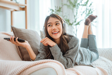 Happy asian woman listening to music from mobile phone while sitting on the the sofa at homes,...