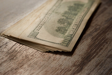 A stack of hundred-dollar bills lies on a wooden table, currency exchange, financial turnover, cash...