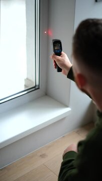 A man measures the temperature of a window in a room using a laser infrared thermometer