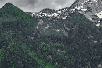 The view depicts a mountain towering over a valley, with lush greenery contrasting the rugged...