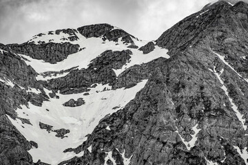 The view depicts a mountain towering over a valley, with lush greenery contrasting the rugged...