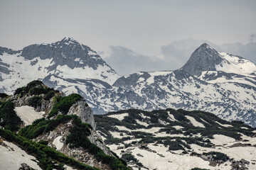 The view depicts a mountain towering over a valley, with lush greenery contrasting the rugged...