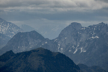 The view depicts a mountain towering over a valley, with lush greenery contrasting the rugged...