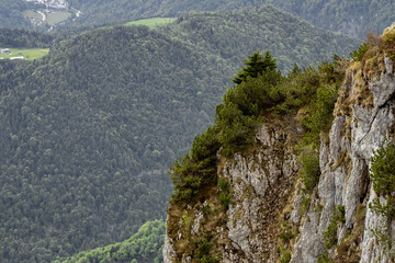 The view depicts a mountain towering over a valley, with lush greenery contrasting the rugged...