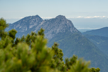 The view depicts a mountain towering over a valley, with lush greenery contrasting the rugged...