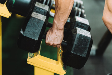 Close up view of a male hand picking up a dumbbell from a rack ina gym