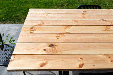 A modern table made of raw wood covered with yacht varnish, standing on the garden terrace.