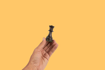 Black male hand holding a black queen chess figure isolated on yellow background