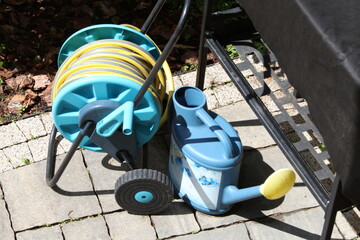 Watering hose on reel, watering can in backyard in spring on stone tile patio. 